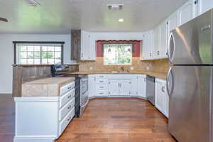 Kitchen featuring plenty of natural light, white cabinetry, dark wood-type flooring, and stainless steel appliances