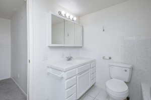 Bathroom featuring tile patterned flooring, tile walls, toilet, and vanity