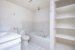 Bathroom with tiled bath, a textured ceiling, toilet, tile patterned floors, and vanity