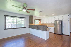 Kitchen with white cabinetry, stainless steel fridge, dark hardwood / wood-style flooring, and kitchen peninsula