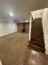 Staircase with brick wall, a wood stove, ceiling fan, and dark hardwood / wood-style floors