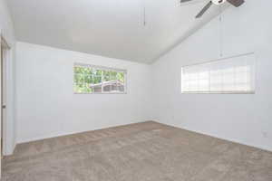 Carpeted empty room with ceiling fan and vaulted ceiling