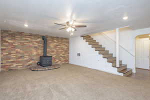 Basement with a wood stove, carpet flooring, brick wall, and ceiling fan