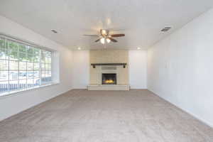 Unfurnished living room with ceiling fan, a fireplace, carpet floors, and a textured ceiling