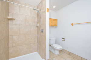 Bathroom featuring tiled shower, tile patterned floors, toilet, and a textured ceiling