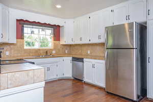 Kitchen with decorative backsplash, appliances with stainless steel finishes, dark hardwood / wood-style flooring, and white cabinets