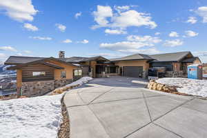 View of front of home featuring a garage, stone siding, a chimney, and driveway