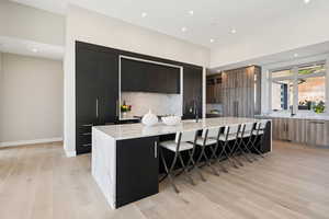 Kitchen featuring modern cabinets, a large island, light wood finished floors, light stone counters, and a breakfast bar