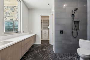 Bathroom with a tile shower, marble finish floor, toilet, and a sink