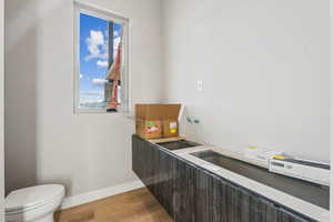 Bathroom with baseboards, plenty of natural light, wood finished floors, and toilet