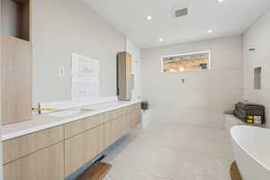 Bathroom featuring visible vents, double vanity, a freestanding bath, a sink, and tile walls