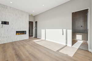 Unfurnished living room featuring a tiled fireplace, light wood-style flooring, recessed lighting, and baseboards