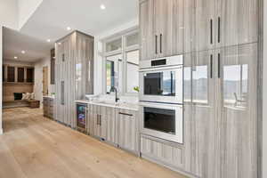 Kitchen with double oven, modern cabinets, light wood finished floors, light countertops, and wine cooler