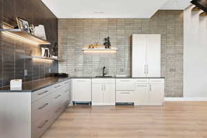 Kitchen with open shelves, dark countertops, light wood-style flooring, and decorative backsplash