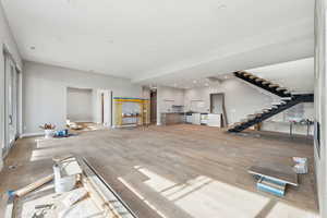 Unfurnished living room with recessed lighting, baseboards, wood finished floors, and stairs