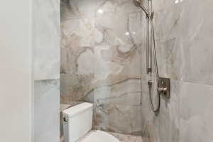 Bathroom featuring toilet and a marble finish shower