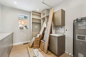 Clothes washing area featuring baseboards, hookup for a washing machine, light wood-style floors, cabinet space, and hookup for an electric dryer