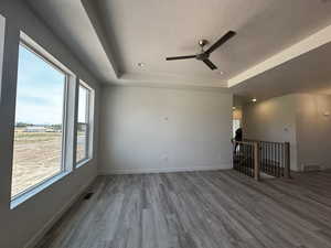 Spare room with a textured ceiling, wood-type flooring, ceiling fan, and a raised ceiling