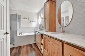 Primary Bathroom with wood-type flooring, tile walls, independent shower and bath, dual bowl vanity, and a textured ceiling