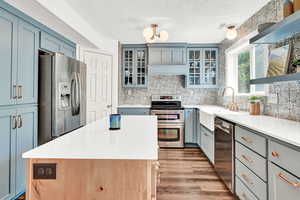 Kitchen with light hardwood / wood-style LVT flooring, a textured ceiling, a center island, backsplash, and appliances with stainless steel finishes