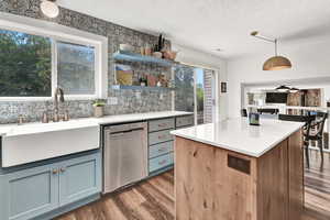 Kitchen with dishwasher, a textured ceiling, dark wood-type LVT flooring, and a healthy amount of sunlight