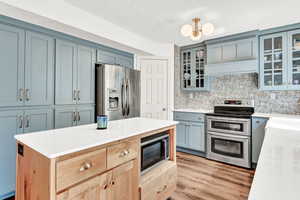 Kitchen with light brown cabinets, tasteful backsplash, light wood-style LVT flooring, stainless steel appliances, and blue cabinets