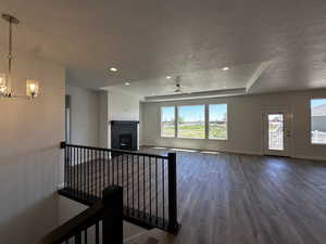 Unfurnished living room with a fireplace, a textured ceiling, ceiling fan with notable chandelier, a tray ceiling, and wood-type flooring