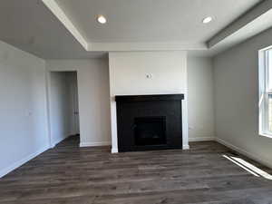 Unfurnished living room with a tray ceiling, a tiled fireplace, hardwood / wood-style flooring, and a healthy amount of sunlight