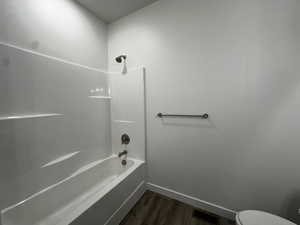 Bathroom with toilet, shower / bathing tub combination, and hardwood / wood-style flooring