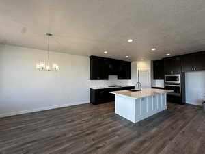 Kitchen with appliances with stainless steel finishes, dark hardwood / wood-style floors, a center island with sink, and a textured ceiling