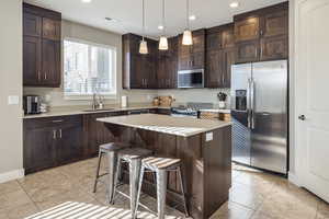 Kitchen with stainless steel appliances, a kitchen island, pendant lighting, a breakfast bar, and sink