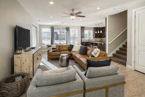 Living room featuring light tile patterned floors, ceiling fan with notable chandelier, and sink