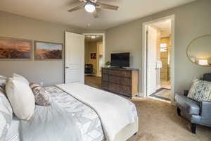 Carpeted bedroom featuring ensuite bath and ceiling fan