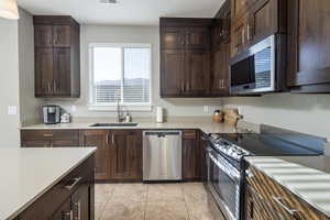 Kitchen with light tile patterned floors, dark brown cabinets, sink, and stainless steel appliances