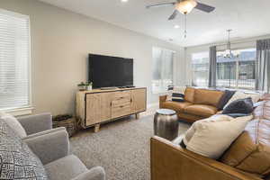 Living room with ceiling fan with notable chandelier, carpet, and a textured ceiling