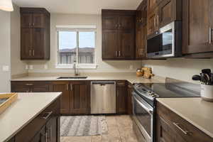 Kitchen with dark brown cabinets, light tile patterned flooring, appliances with stainless steel finishes, and sink