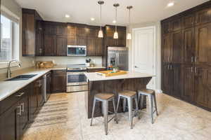 Kitchen featuring light tile patterned flooring, stainless steel appliances, sink, a center island, and dark brown cabinetry