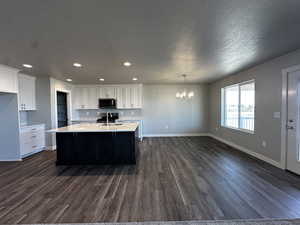 Kitchen featuring dark hardwood / wood-style flooring, decorative backsplash, white cabinets, and a center island with sink