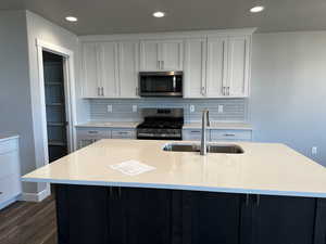 Kitchen with appliances with stainless steel finishes, hardwood / wood-style floors, sink, light stone countertops, and an island with sink