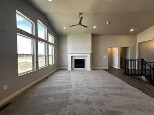 Unfurnished living room featuring dark colored carpet, a brick fireplace, ceiling fan, and vaulted ceiling