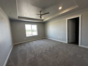 Unfurnished room featuring ceiling fan, a textured ceiling, a tray ceiling, and carpet flooring