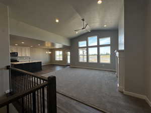 Living room with a healthy amount of sunlight, dark carpet, ceiling fan with notable chandelier, and vaulted ceiling