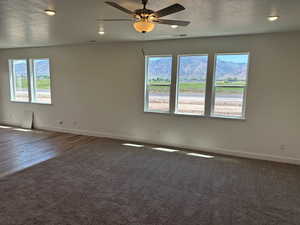 Carpeted empty room with a textured ceiling, a mountain view, a healthy amount of sunlight, and ceiling fan