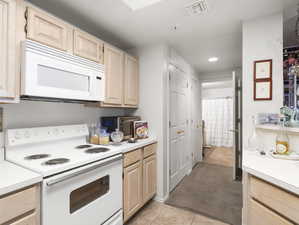 Kitchen featuring light colored carpet, light brown cabinets, and white appliances