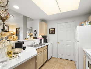 Kitchen featuring light tile patterned floors, white appliances, light brown cabinets, and sink