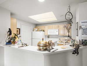 Kitchen with light brown cabinetry, kitchen peninsula, white appliances, and a skylight