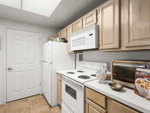 Kitchen with light tile patterned flooring, light brown cabinets, and white appliances