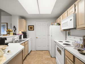 Kitchen with light tile patterned flooring, a skylight, white appliances, light brown cabinetry, and sink