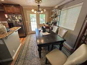 Dining room featuring a chandelier, light wood-type flooring, crown molding, and a textured ceiling