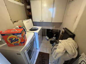 Clothes washing area with cabinets, tile patterned floors, and washing machine and dryer